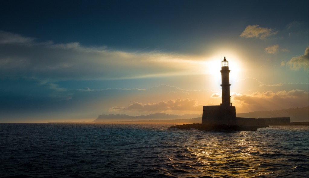 Spectacular sunset shot of a lit lighthouse by the sea.