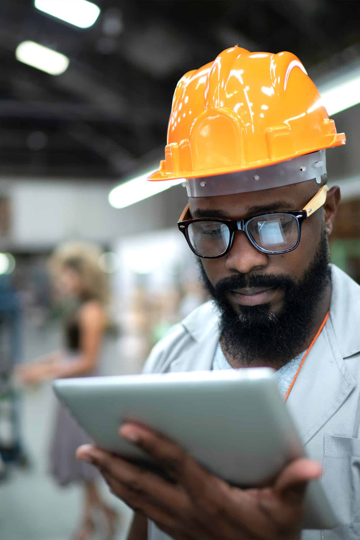 A worker in an orange hard hat and glasses reads information on a tablet, using the guide to decreasing downtime in an industrial setting.