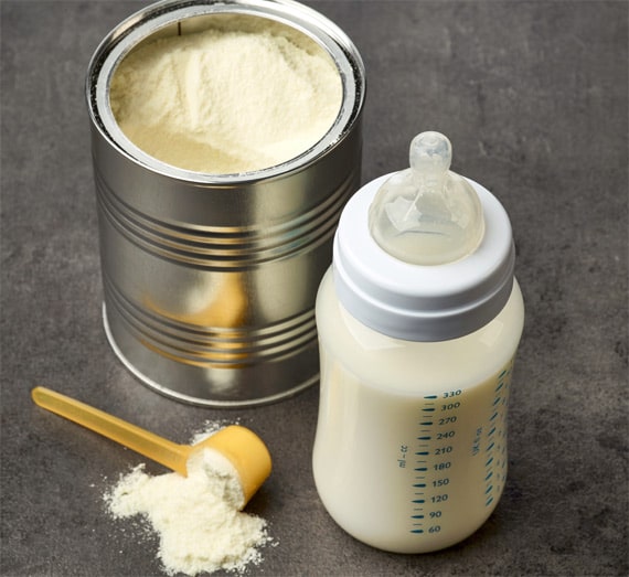 An open tin can of infant formula, a yellow scoop with some powder, and a baby bottle filled with prepared formula—perfect components for any new parent's value calculator.