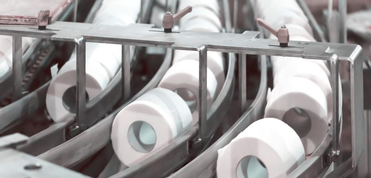 Close-up of a toilet paper manufacturing assembly line, showing multiple rolls of toilet paper moving along three metal conveyor belts, efficiently counted by a value calculator to ensure precision.
