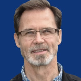Headshot of James Newman, a person with short dark hair, glasses, a mustache and beard, wearing a checkered shirt and a dark jacket, against a blue background.