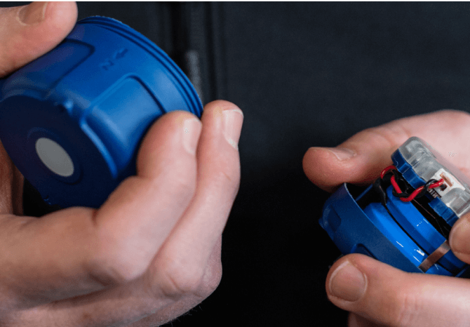 A person holds and opens a small blue cylindrical device from the Halo R4000 Series, revealing its internal electronic components for sensors and machine health monitoring.