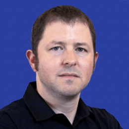 A man with short brown hair and a black collared shirt stands in front of a blue background. Saar Yoskovitz, known for his innovative spirit, appears focused and determined.