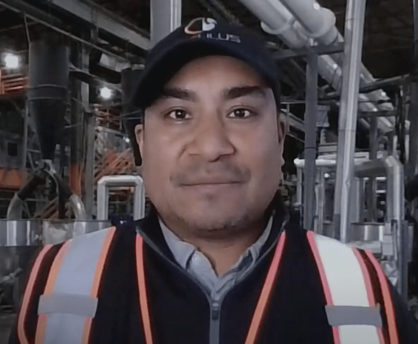 Carlos Figueroa, the Maintenance Manager at Circulus, stands in an industrial setting with machinery and pipes in the background, wearing a cap and a safety vest.