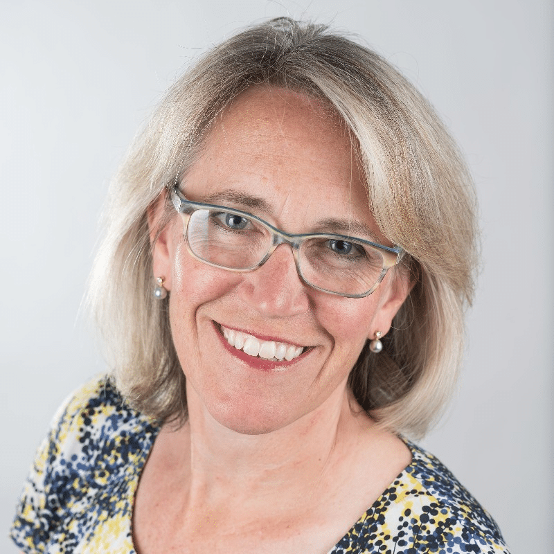 A woman with shoulder-length blonde hair, wearing glasses and a multicolored top, smiles at the camera against a plain background, embodying the spirit of an ISV journey on Microsoft Azure.